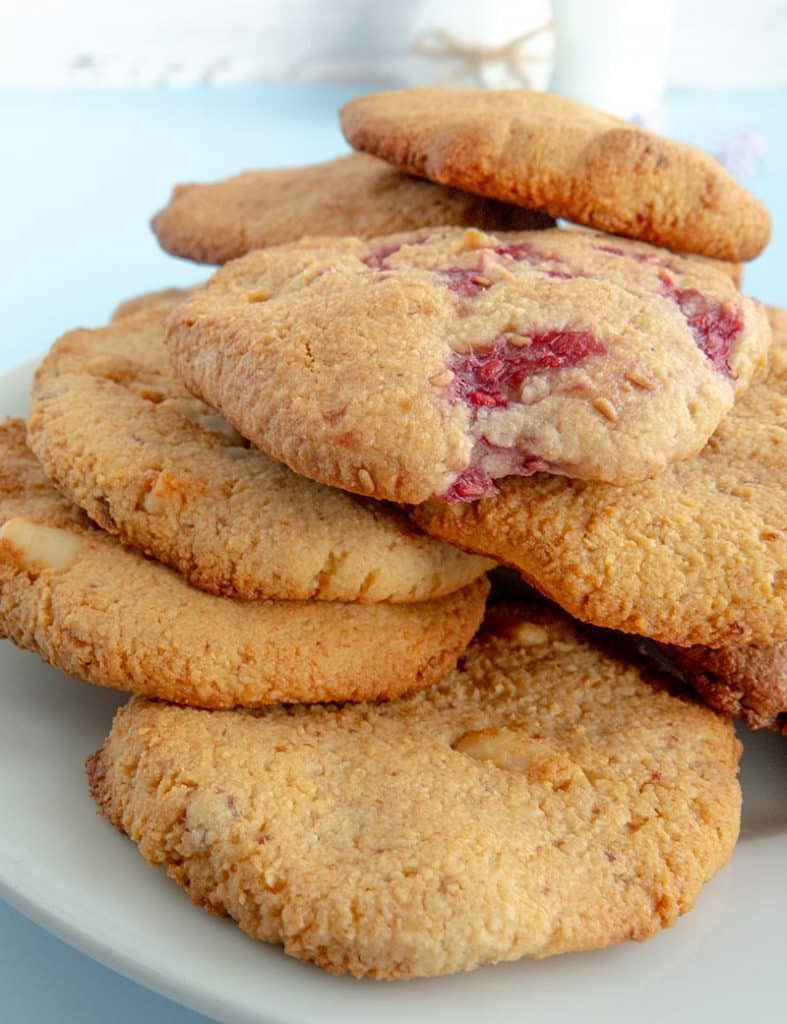 Selbstgebackene Mandelmehl-Macadamia-Kekse gestapelt auf einem Teller mit frischen Himbeeren