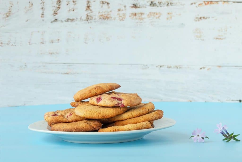 Frisch gebackene Mandelmehl-Kekse mit Macadamia und Himbeeren auf einem Teller