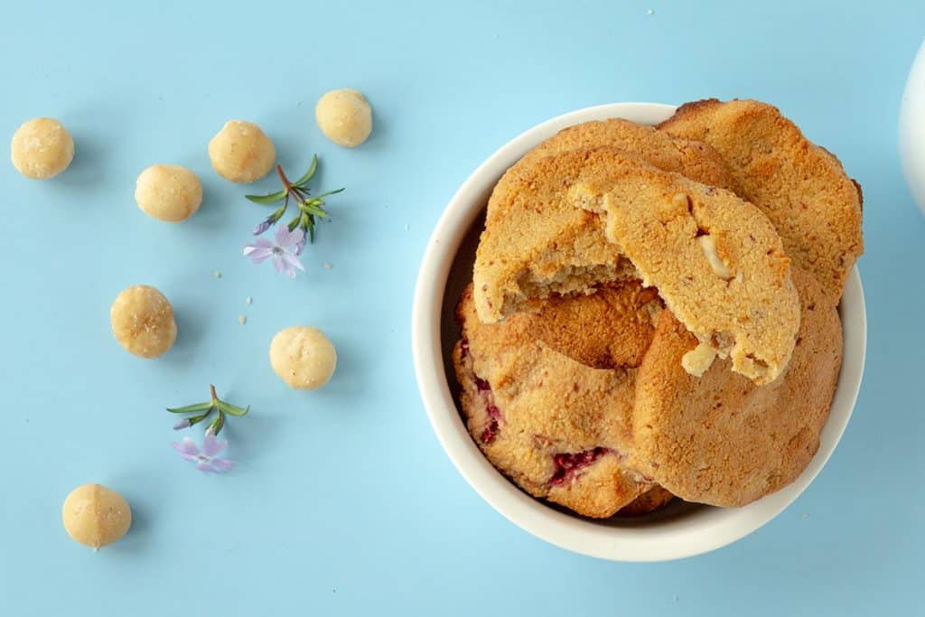 Mandelmehl-Kekse von oben in einer Schale mit Macadamia-Stücken und Himbeeren