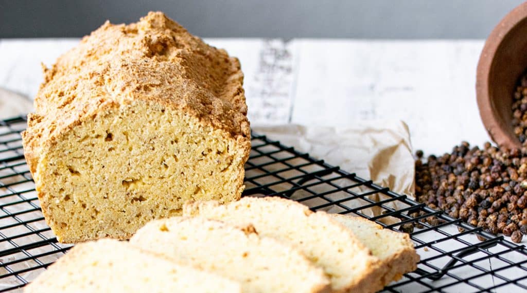 Angeschnittenes Mandelmehlbrot mit Ei auf einem Abkühlgitter, davor lieben 4 geschnittene Scheiben. 