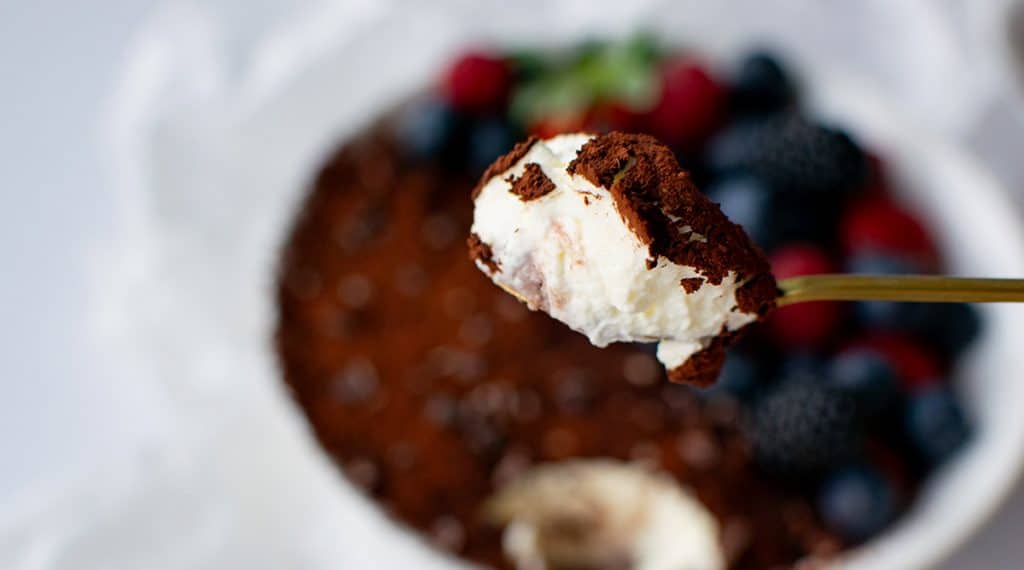Löffel mit cremigem Tiramisu und Kakao im Vordergrund