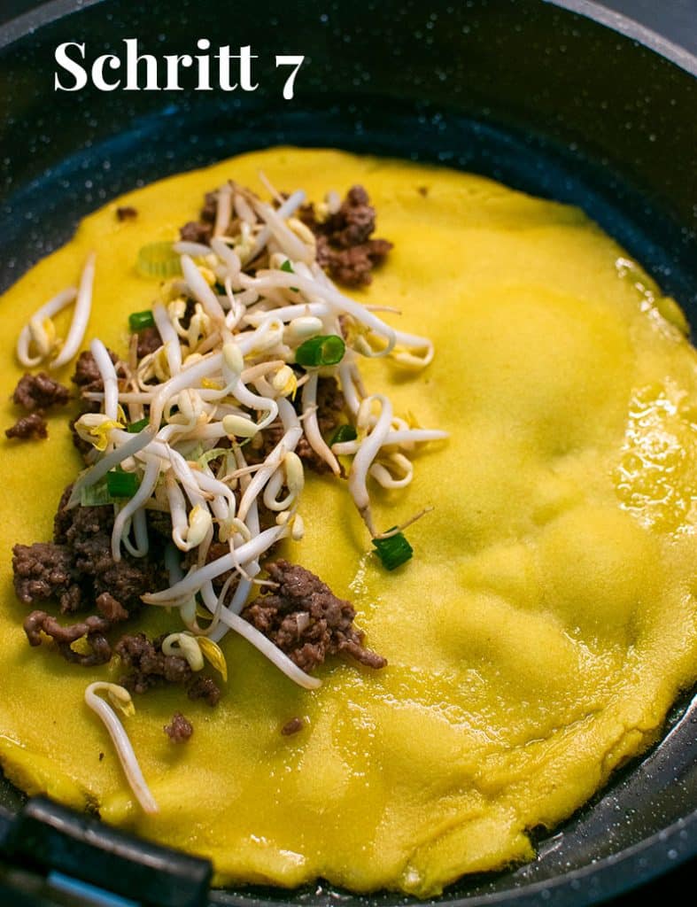Banh Chaevv in einer Pfanne, auf der linken Hälfte die Füllung aus Hackfleisch, Sprossen und Frühlingsziebeln.