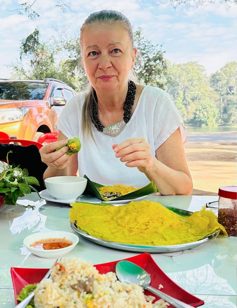 Ich - Inga - in einem kleinen Restaurant in Siem Reap, Kambodscha. Dort esse ich gerade original Banh Chhaev. Auf dem Teller vor mir mehrere von diesen köstlichen Pfannkuchen auf Bananenblättern. 