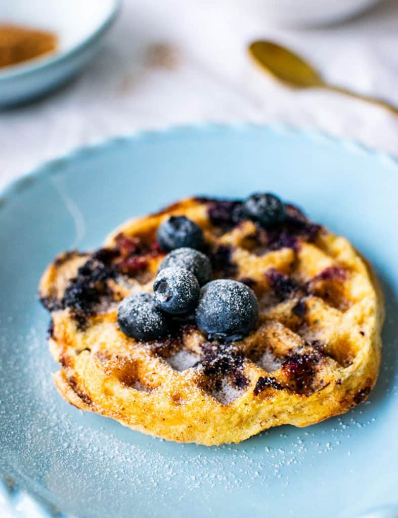 Mandelmehl-Waffel, die zusammen mit Beeren im Teig gebacken wurde. Oben auf der Waffel befinden sich ein paar frische Beeren, die mit Erythrit bestäubt sind, was wie Puderzucker aussieht. 