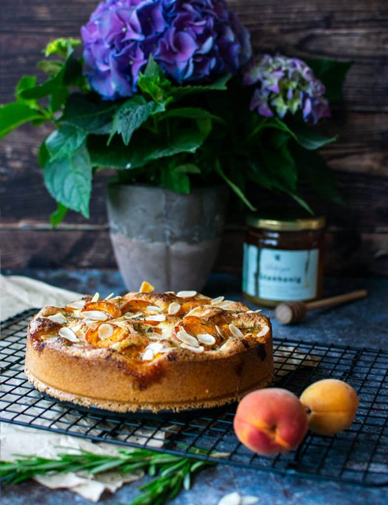 Mandelmehlkuchen mit Aprikosen, Rosmarin und Mandelblättchen auf einem Kuchengitter