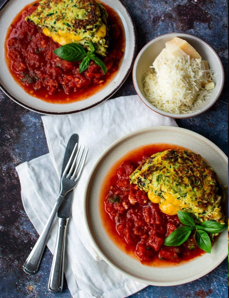 Low-Carb Zucchini-Puffer mit Käse und Tomatensauce angerichtet mit frischem Basilikum aus der Vogelperspektive.