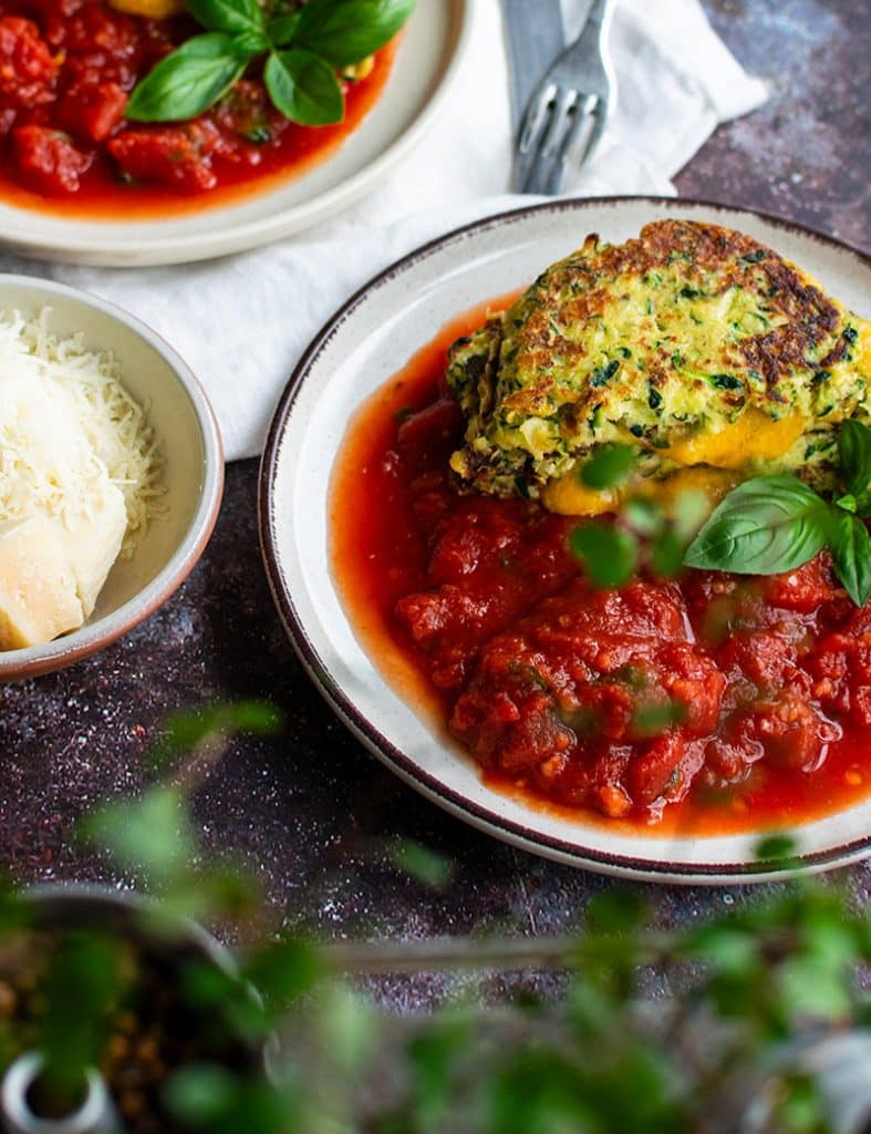 Goldbraune Zucchini-Puffer mit geschmolzener Käsefüllung auf würziger Tomatensauce und frischem Basilikum.